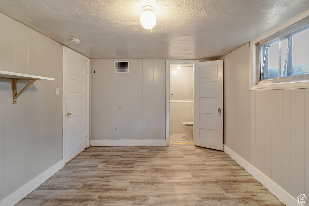 Unfurnished bedroom with a textured ceiling, light wood-type flooring, wood walls, and ensuite bath