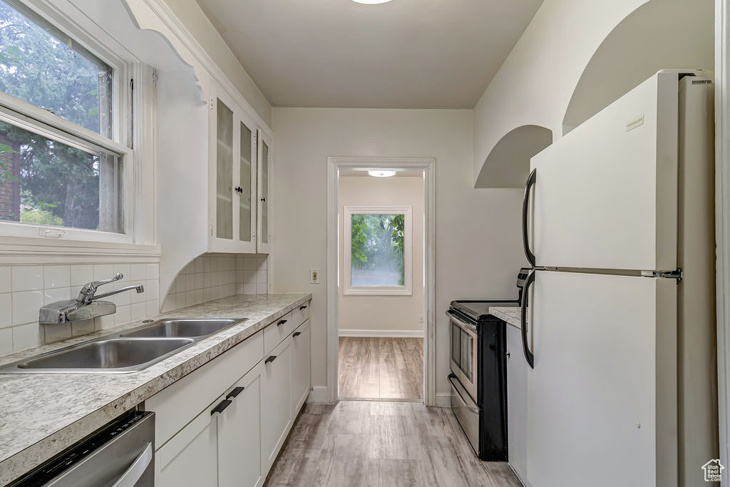 Kitchen with white cabinets, sink, light hardwood / wood-style flooring, backsplash, and stainless steel appliances