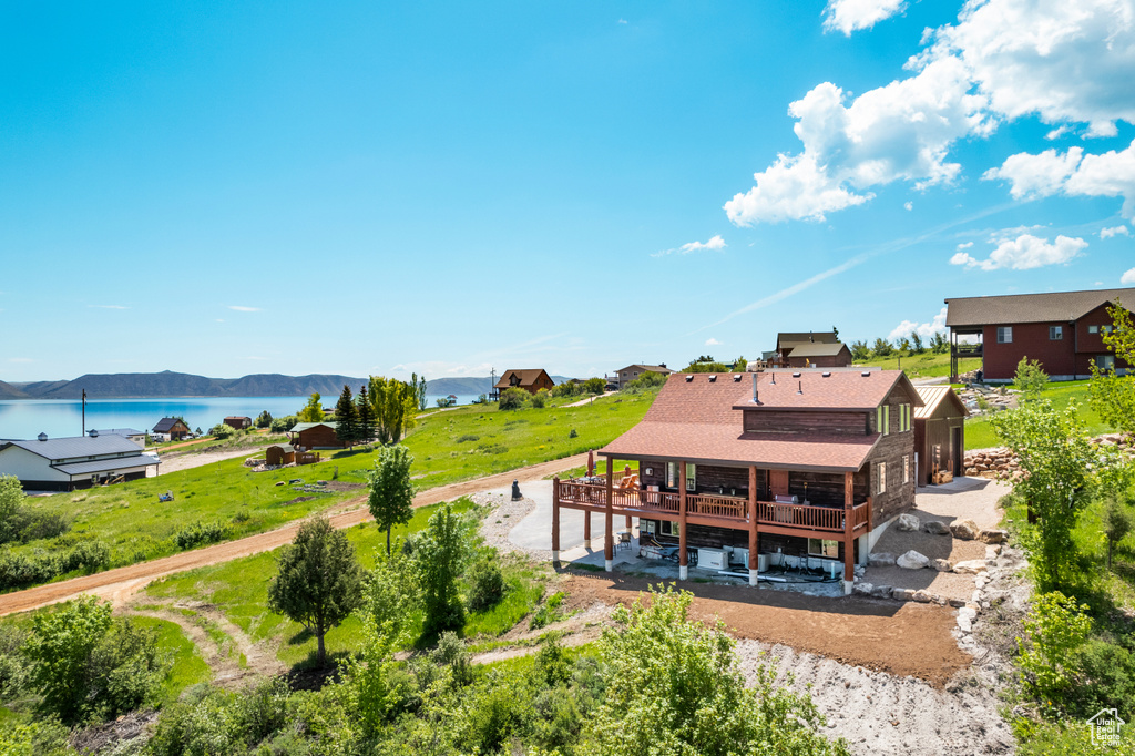 Back of property featuring a deck with water view, roof with shingles, and a patio area