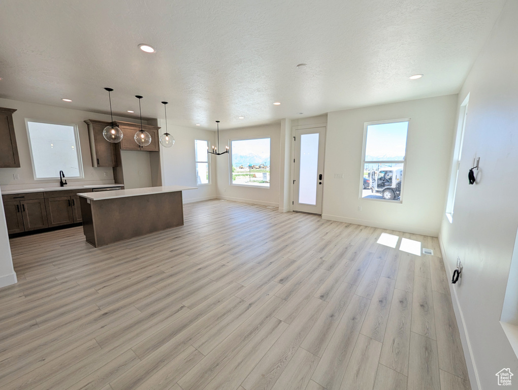 Kitchen with pendant lighting, light wood-type flooring, an inviting chandelier, a center island, and sink