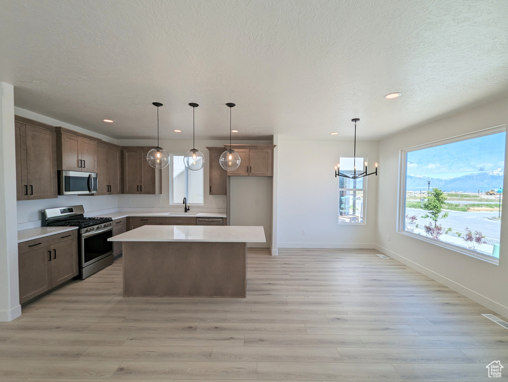 Kitchen featuring hanging light fixtures, sink, appliances with stainless steel finishes, a center island, and light hardwood / wood-style floors