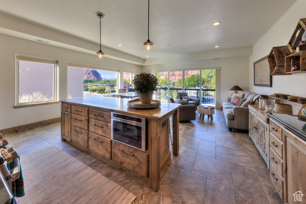Kitchen with hanging light fixtures, a healthy amount of sunlight, a kitchen island, and stainless steel oven