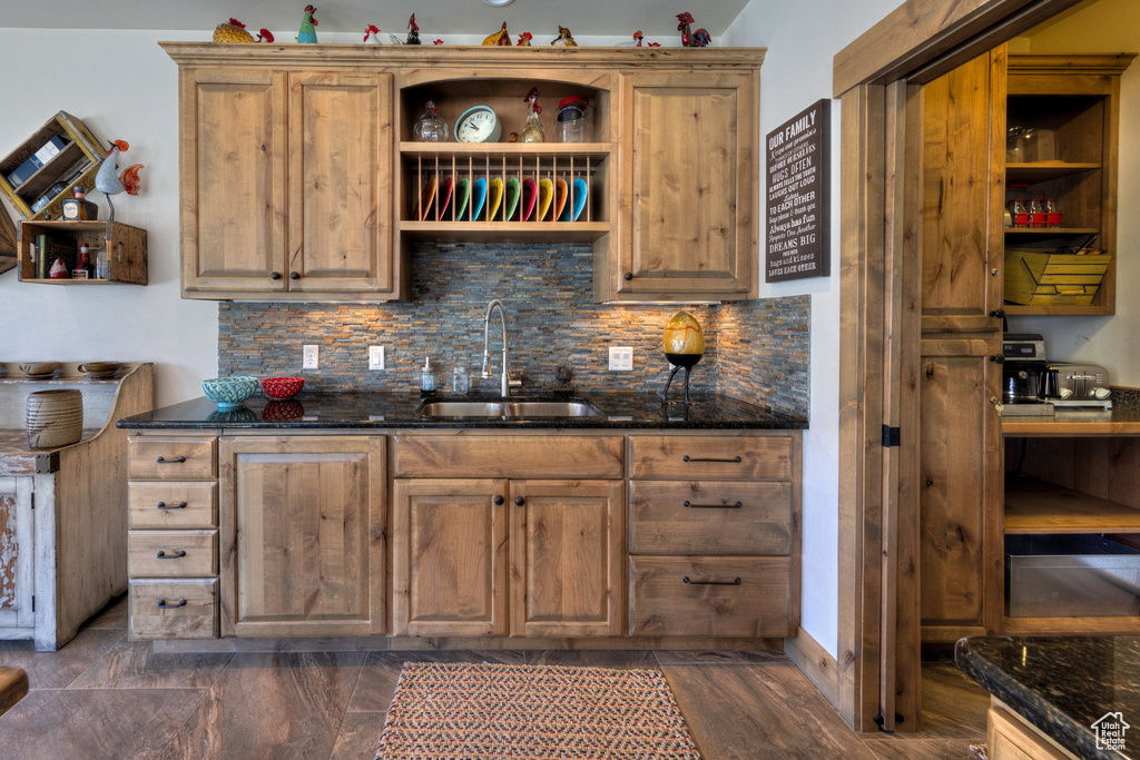 Kitchen with dark stone counters, decorative backsplash, sink, and dark wood-type flooring