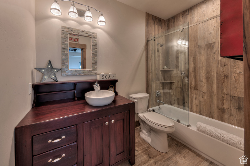 Full bathroom featuring hardwood / wood-style floors, shower / bath combination with glass door, toilet, and vanity