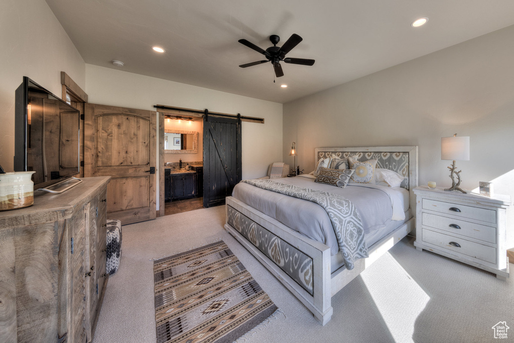 Bedroom featuring ceiling fan, ensuite bath, light carpet, and a barn door