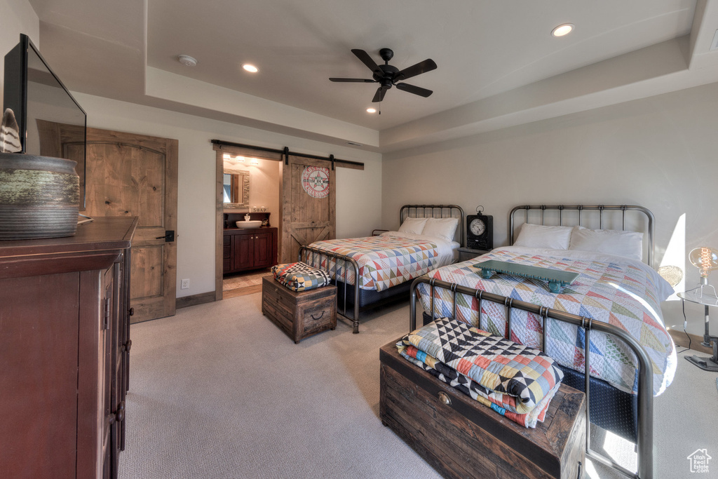 Bedroom featuring ensuite bath, ceiling fan, a raised ceiling, and a barn door