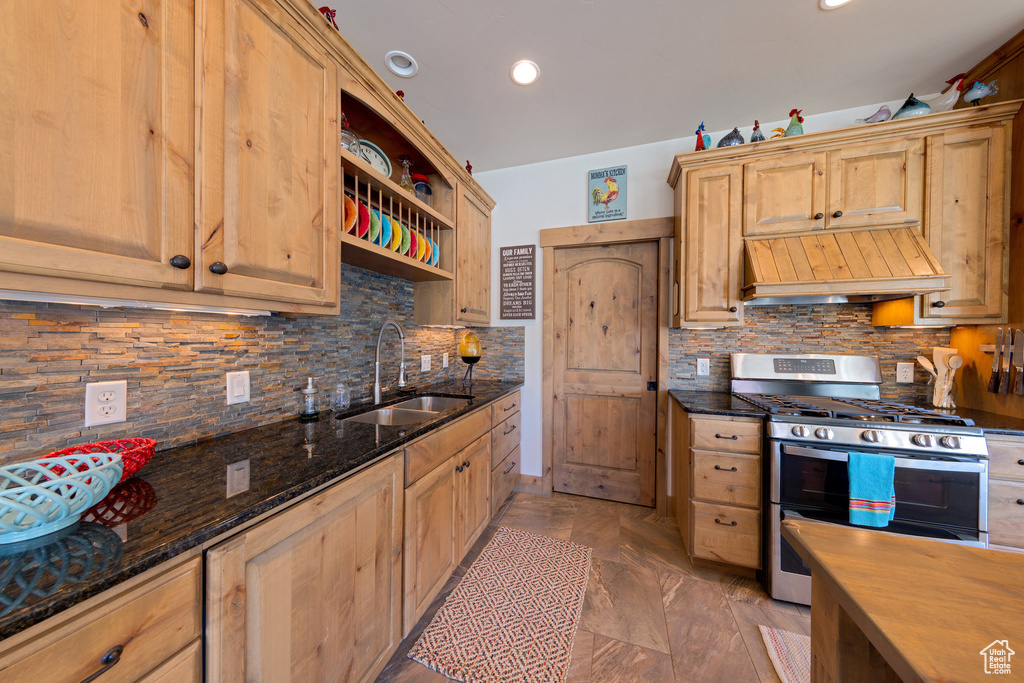 Kitchen featuring premium range hood, sink, backsplash, range with two ovens, and dark stone counters