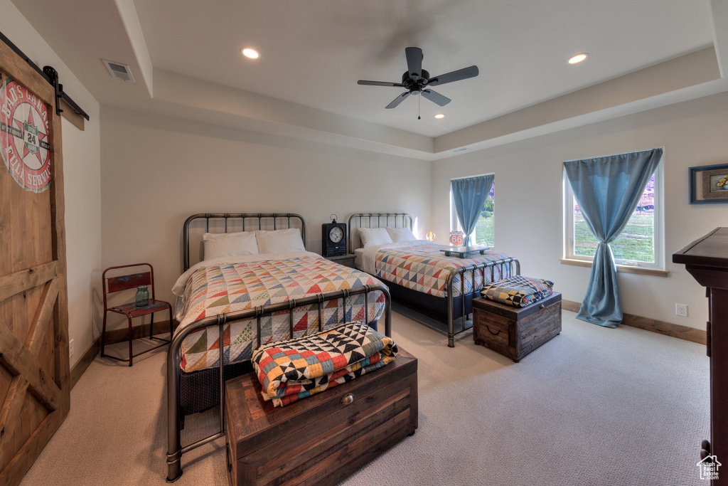 Bedroom with ceiling fan, light colored carpet, a raised ceiling, and a barn door