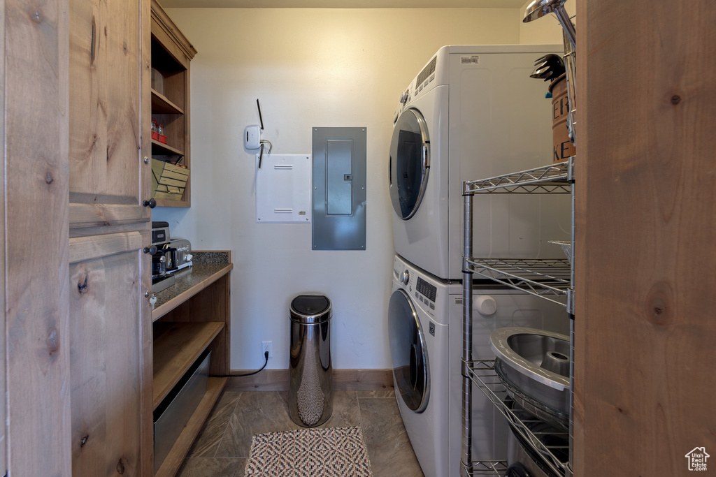 Laundry area featuring electric panel, tile patterned flooring, and stacked washing maching and dryer