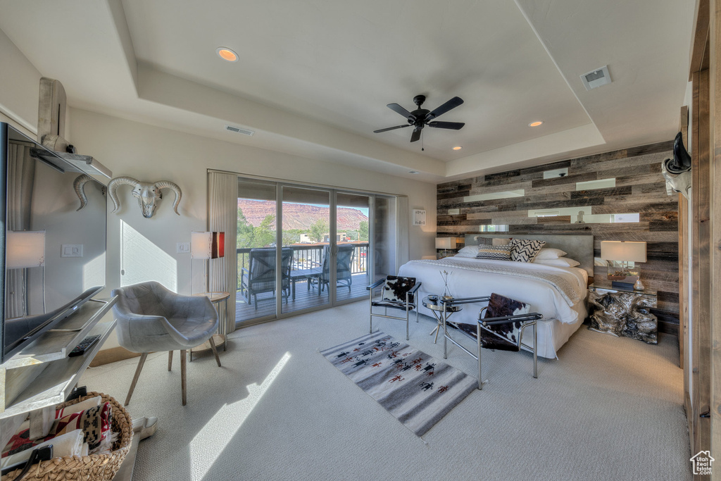 Bedroom featuring a tray ceiling, access to exterior, wood walls, light carpet, and ceiling fan