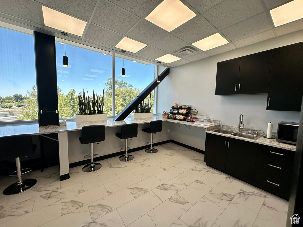 Kitchen featuring a breakfast bar, a drop ceiling, hanging light fixtures, and sink