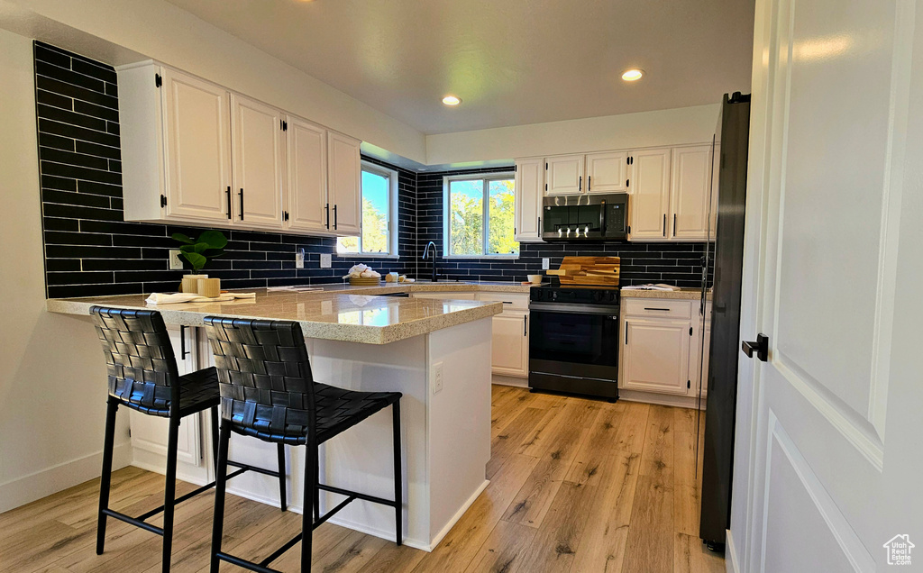 Kitchen with light hardwood / wood-style floors, white cabinetry, kitchen peninsula, stainless steel refrigerator, and black electric range oven