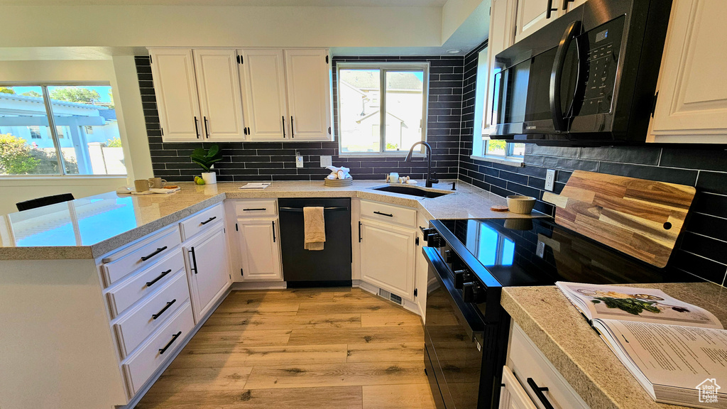 Kitchen with sink, backsplash, white cabinetry, black appliances, and light hardwood / wood-style floors