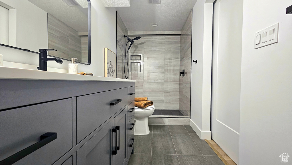 Bathroom featuring a textured ceiling, tiled shower, vanity, and toilet