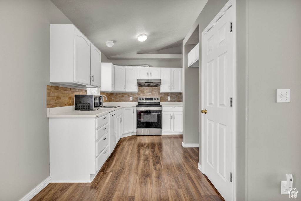 Kitchen featuring vaulted ceiling, dark wood-type flooring, stainless steel appliances, and white cabinets