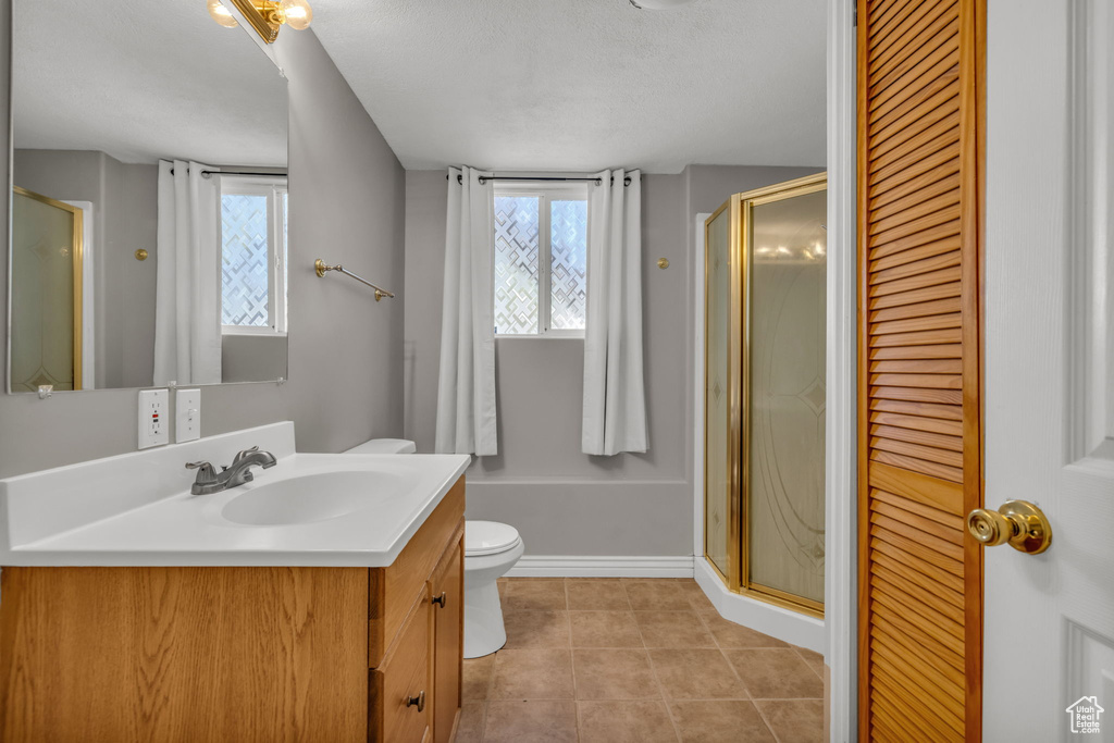 Bathroom with vanity, a shower with shower door, toilet, and a healthy amount of sunlight