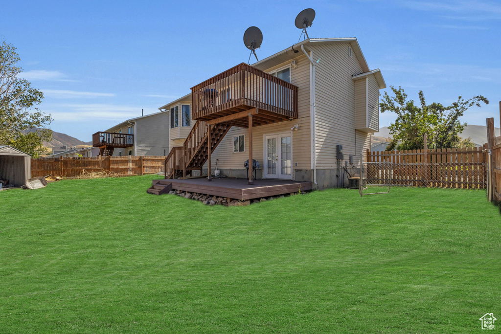 Back of property featuring a lawn, a storage shed, a wooden deck, and french doors