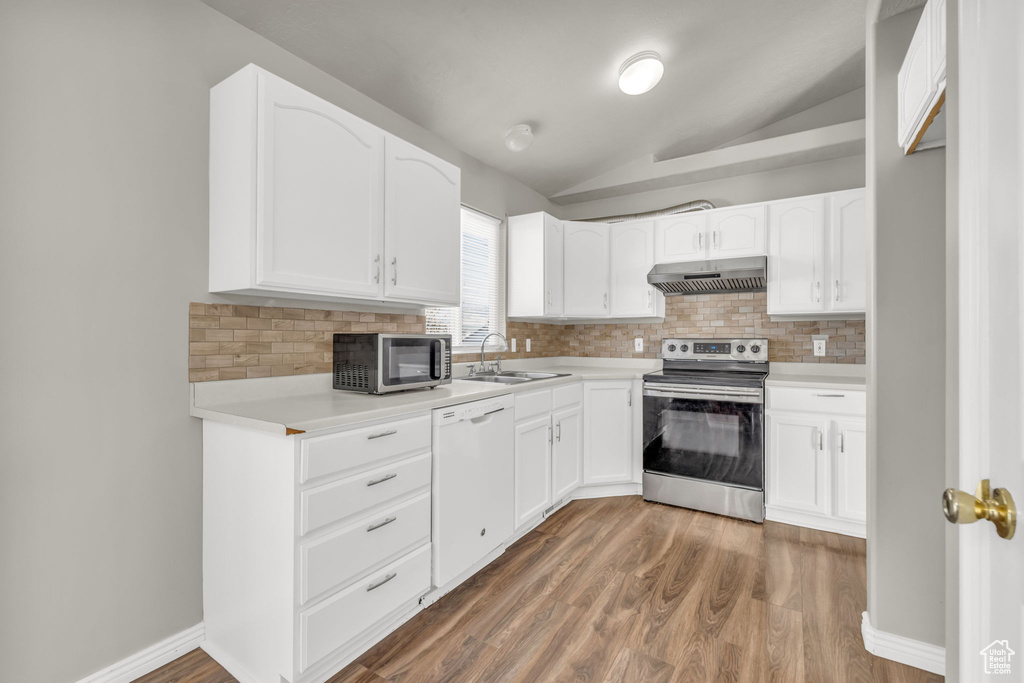 Kitchen featuring appliances with stainless steel finishes, decorative backsplash, dark wood-type flooring, white cabinets, and lofted ceiling