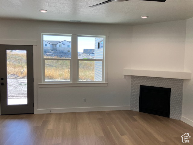 Unfurnished living room featuring ceiling fan, a textured ceiling, light wood-type flooring, and a tile fireplace