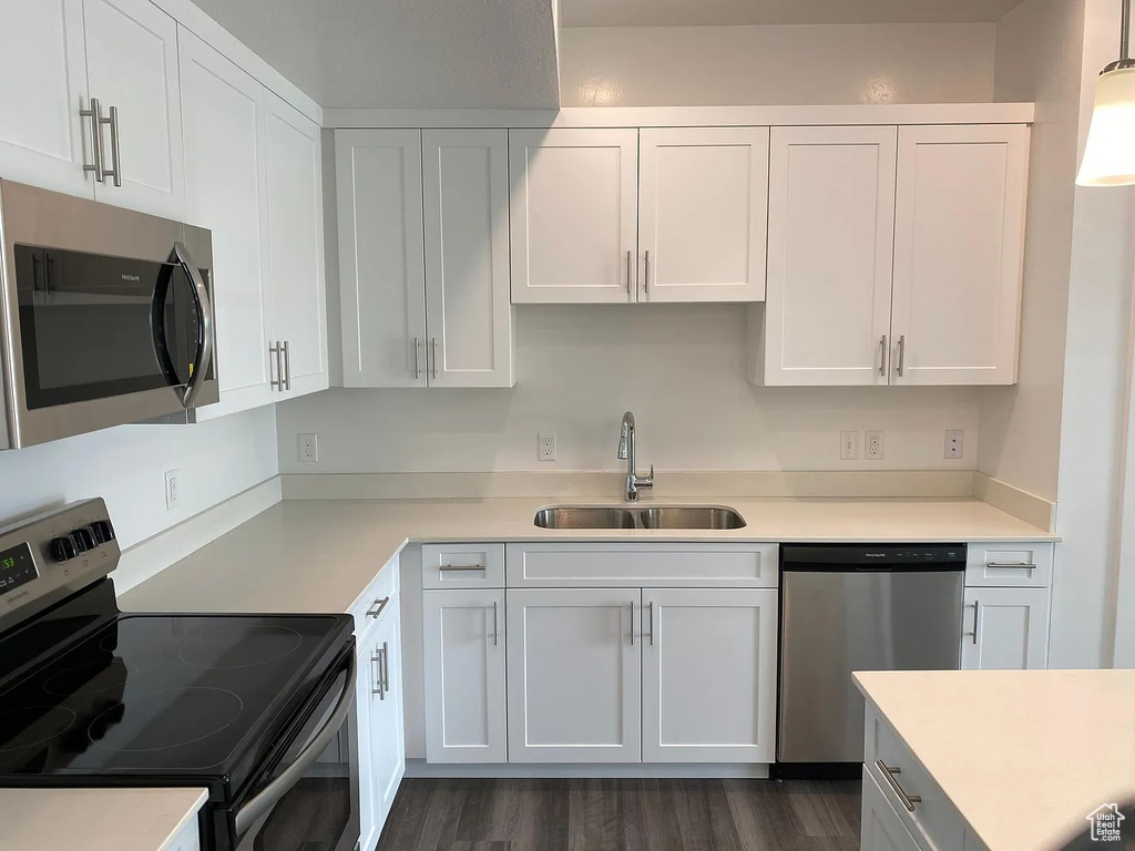 Kitchen featuring dark wood-type flooring, sink, white cabinets, stainless steel appliances, and decorative light fixtures