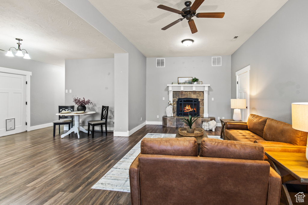 Living room featuring a textured ceiling, ceiling fan with notable chandelier, dark hardwood / wood-style flooring, and a tile fireplace