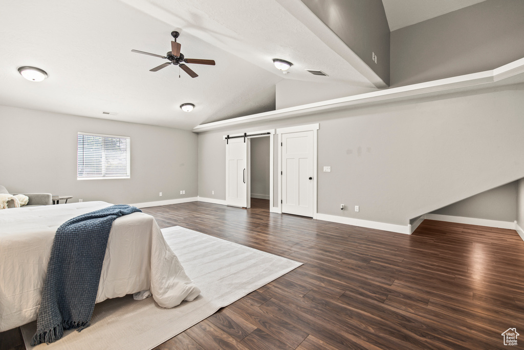 Bedroom with ceiling fan, dark hardwood / wood-style floors, a barn door, and high vaulted ceiling