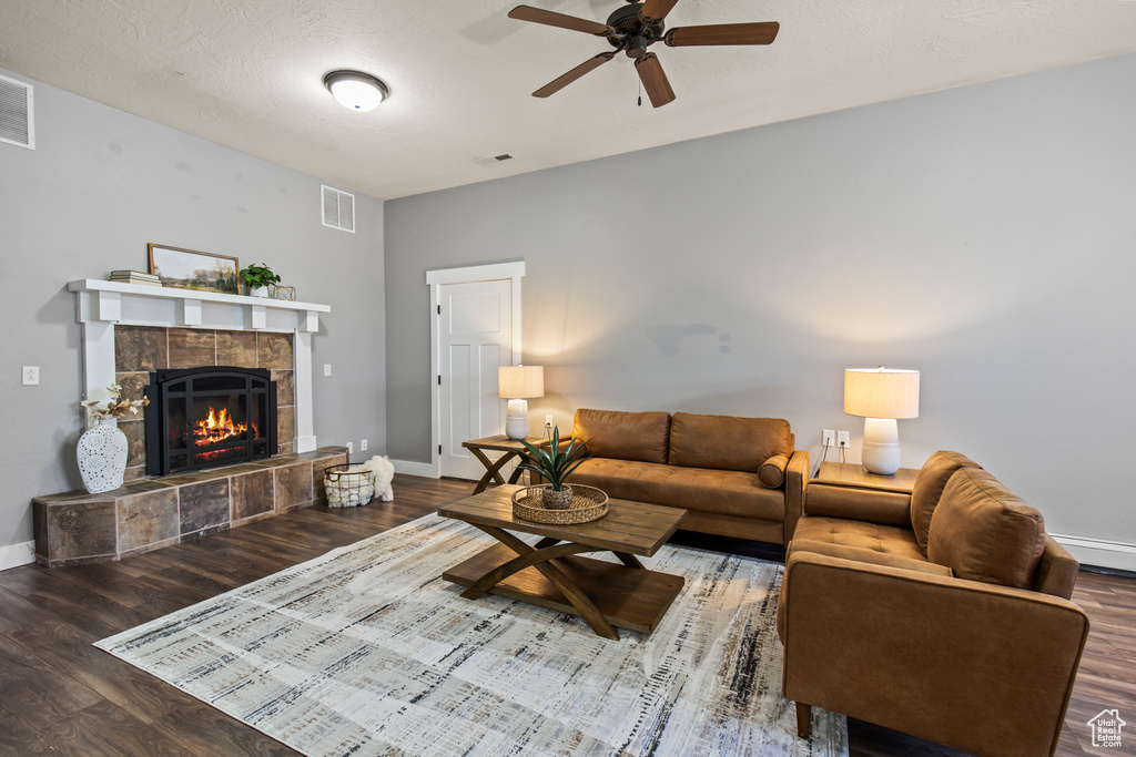 Living room featuring ceiling fan, a textured ceiling, dark wood-type flooring, and a tile fireplace