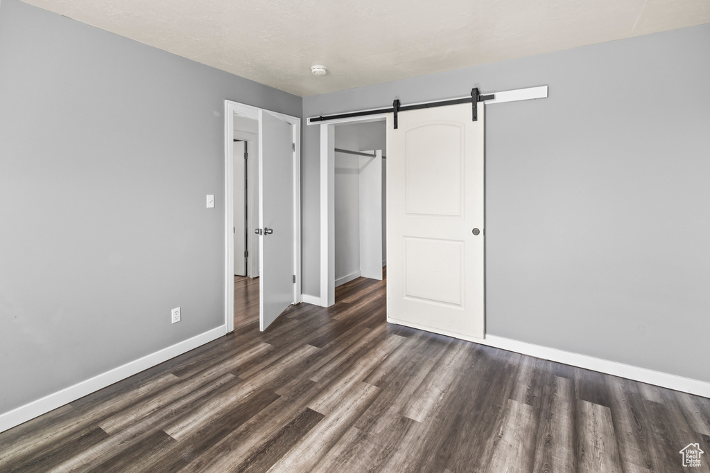 Unfurnished bedroom featuring a closet, dark hardwood / wood-style floors, and a barn door