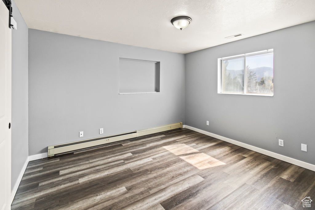 Spare room featuring a baseboard heating unit, hardwood / wood-style flooring, and a barn door