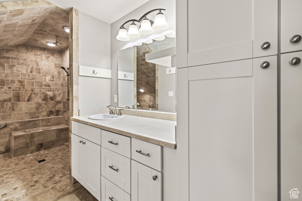 Bathroom featuring vaulted ceiling, vanity, and a tile shower