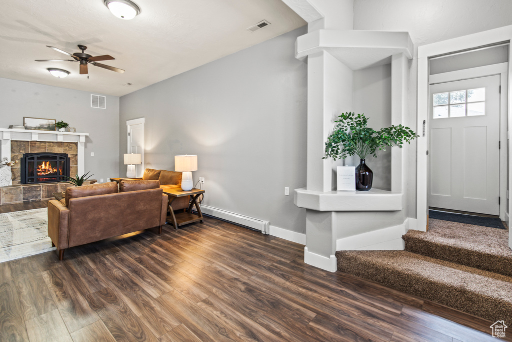 Living room with ceiling fan, baseboard heating, dark hardwood / wood-style flooring, and a tile fireplace