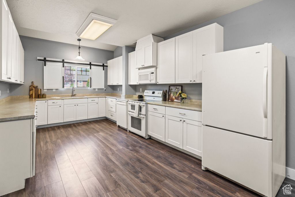 Kitchen with white cabinetry, dark wood-type flooring, a barn door, white appliances, and pendant lighting