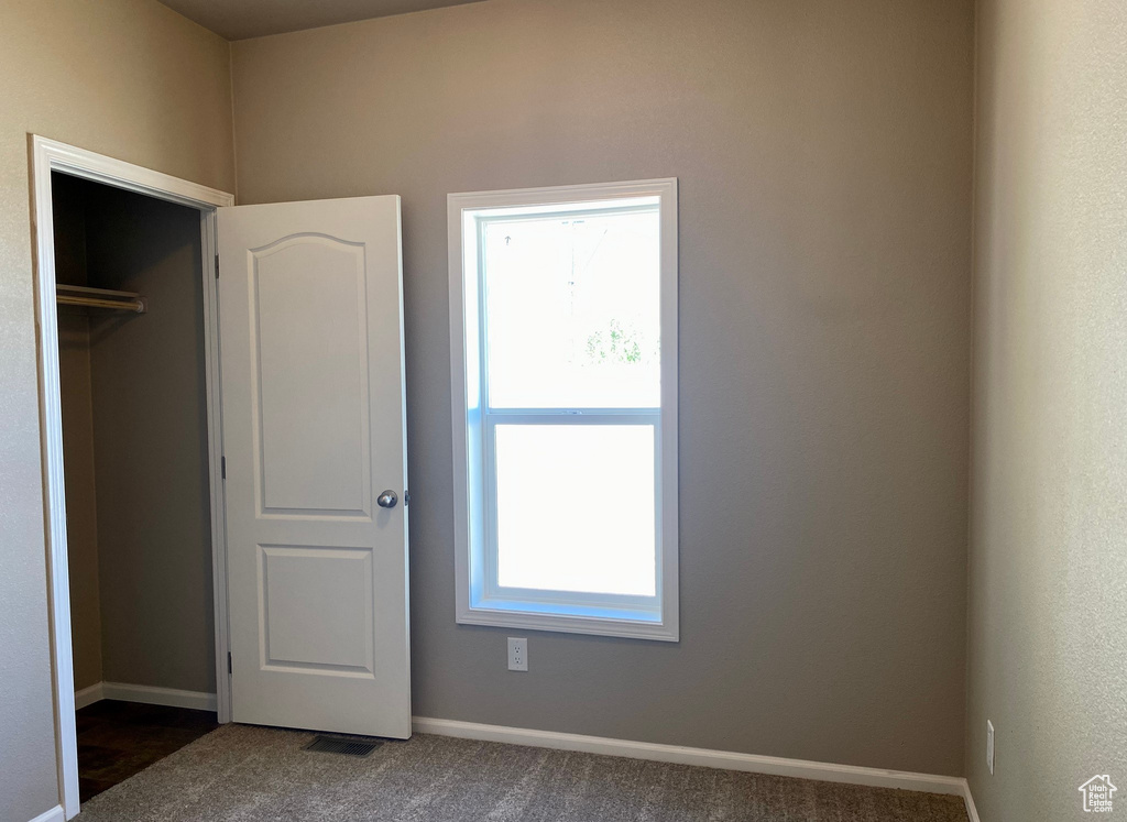 Unfurnished bedroom with dark carpet, a closet, and multiple windows