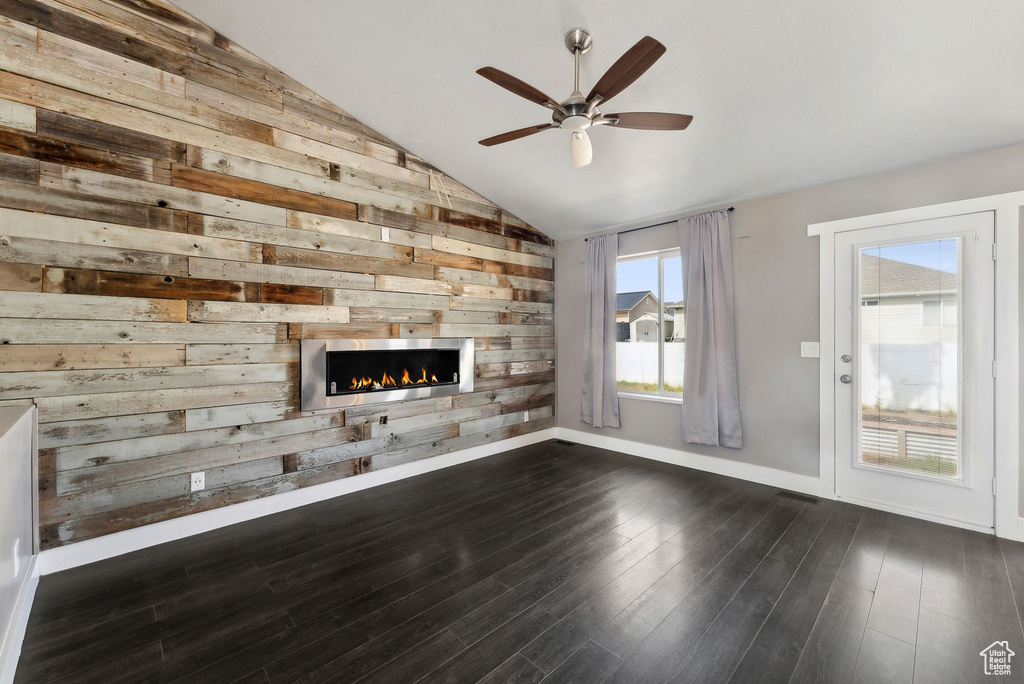 Unfurnished living room with lofted ceiling, wood walls, dark wood-type flooring, and ceiling fan