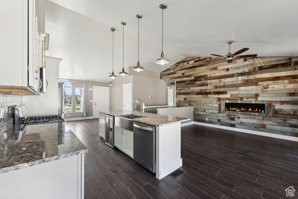 Kitchen featuring sink, white cabinets, wood walls, a center island with sink, and decorative light fixtures