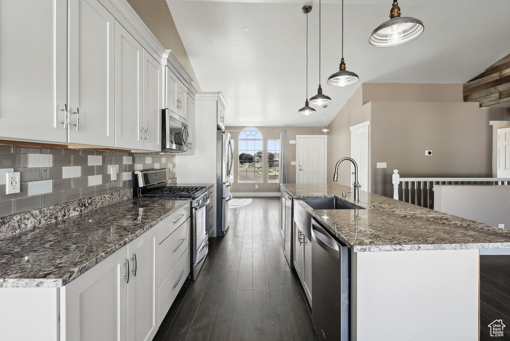 Kitchen with white cabinets, decorative light fixtures, a kitchen island with sink, stainless steel appliances, and vaulted ceiling