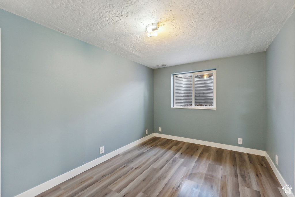 Empty room with a textured ceiling and light hardwood / wood-style floors