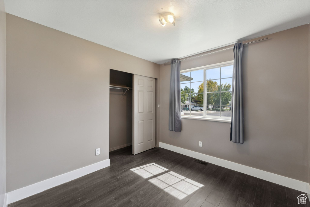 Unfurnished bedroom featuring a closet and dark wood-type flooring