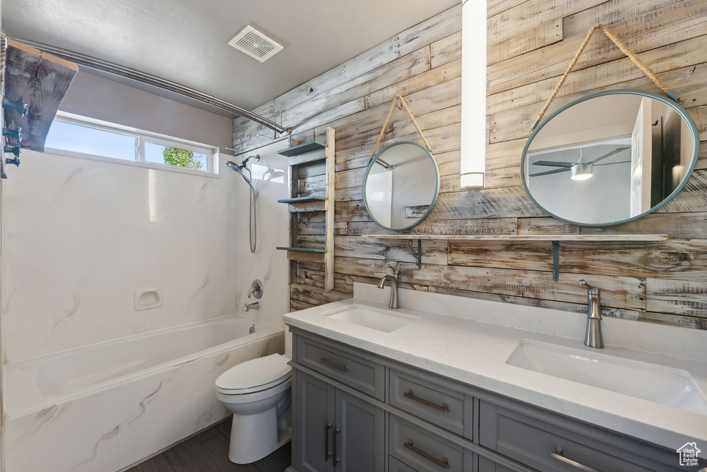 Full bathroom with wood walls, shower / bath combination, vanity, and toilet