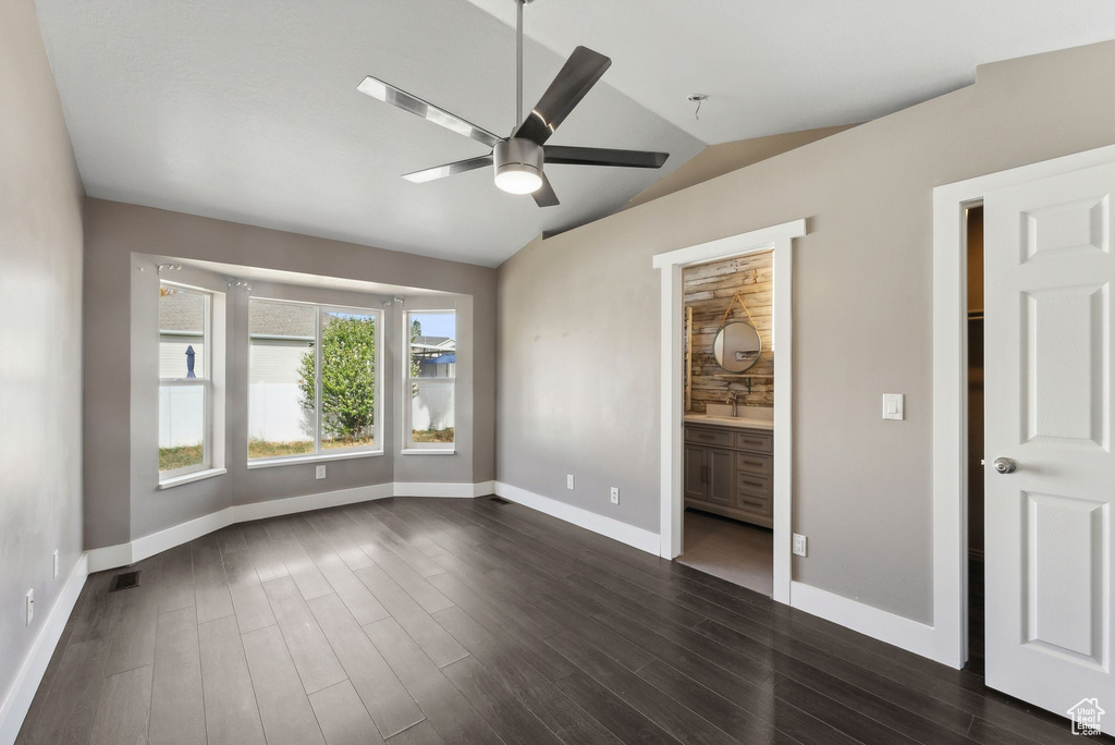 Unfurnished bedroom with ceiling fan, ensuite bathroom, dark hardwood / wood-style floors, and vaulted ceiling