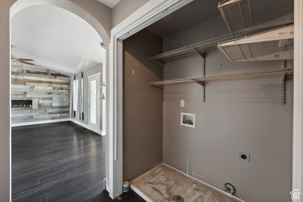 Laundry area featuring a fireplace, ceiling fan, electric dryer hookup, wooden walls, and dark hardwood / wood-style floors