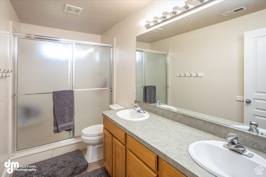 Bathroom with a textured ceiling, walk in shower, tile patterned floors, vanity, and toilet