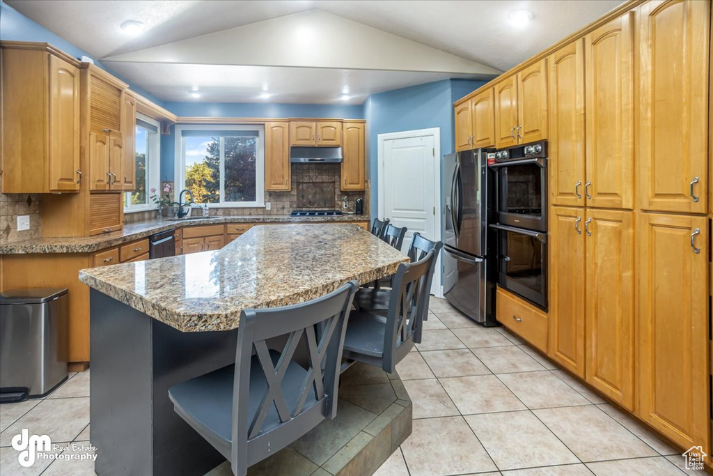 Kitchen with light tile patterned flooring, vaulted ceiling, a kitchen island, black appliances, and sink