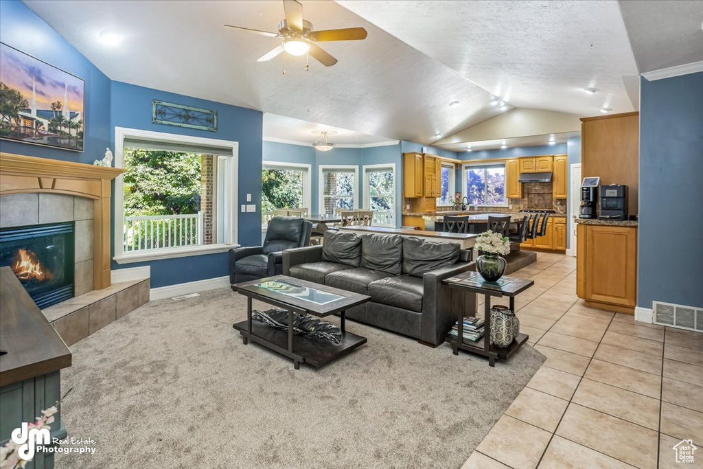 Tiled living room featuring a fireplace, ornamental molding, lofted ceiling, and ceiling fan