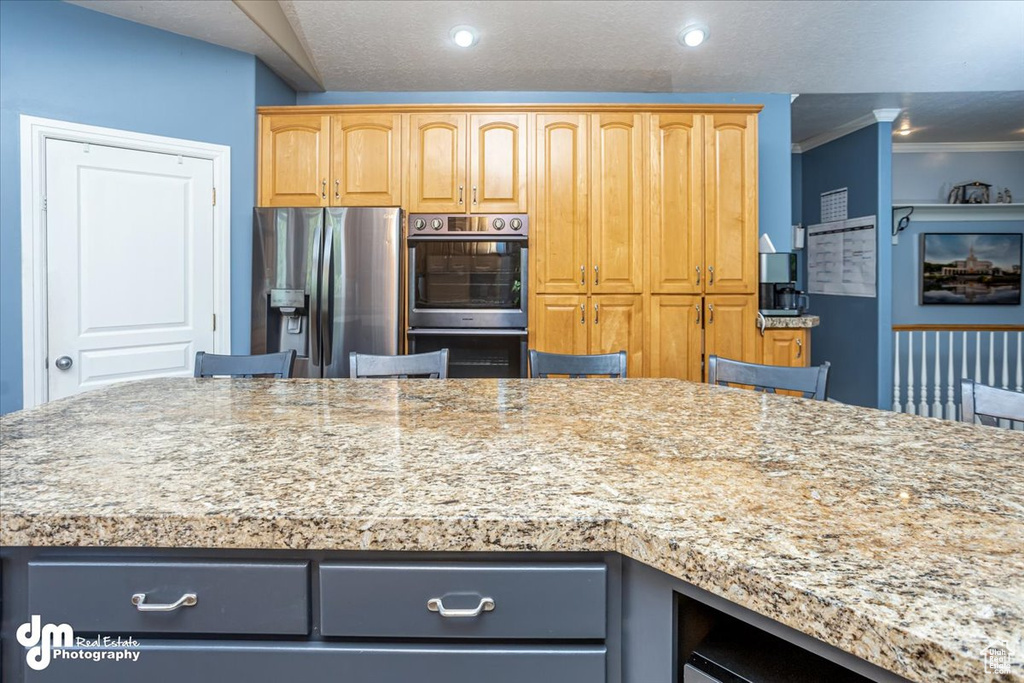 Kitchen with light stone counters, a center island, a breakfast bar area, appliances with stainless steel finishes, and ornamental molding