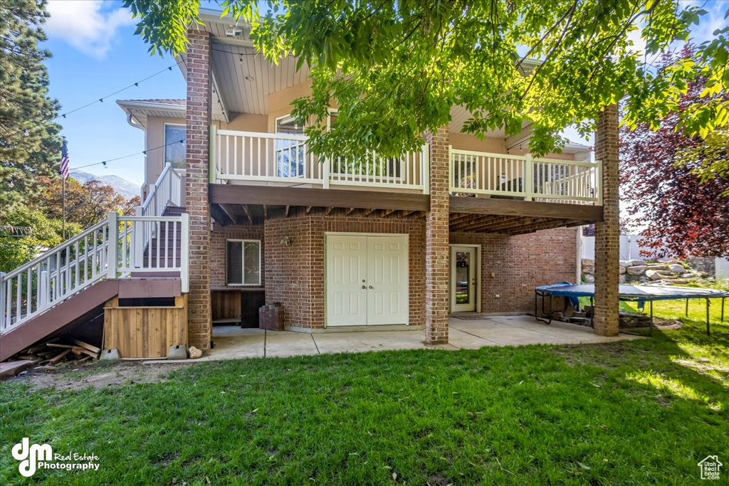 Back of house with a wooden deck, a trampoline, a patio area, and a yard