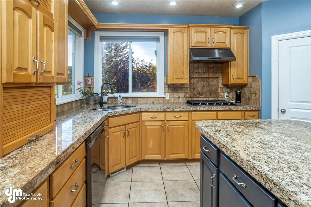 Kitchen with sink, stainless steel gas cooktop, dishwasher, light stone countertops, and decorative backsplash