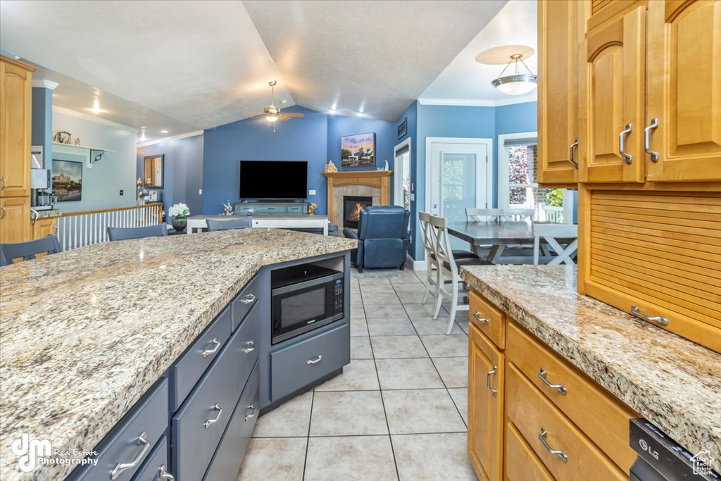 Kitchen featuring light stone counters, stainless steel microwave, vaulted ceiling, and crown molding