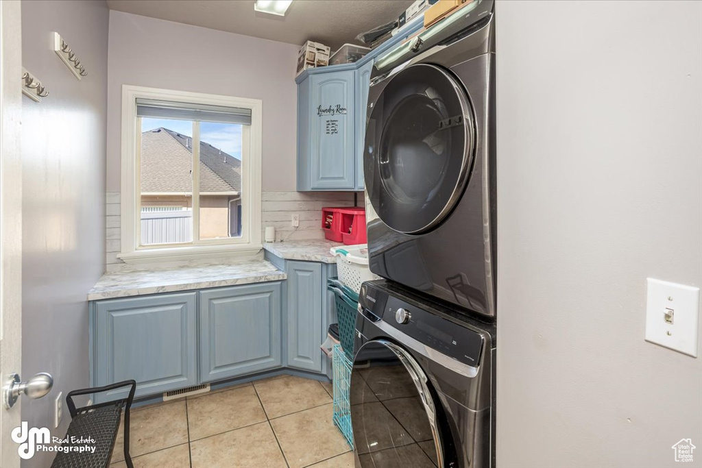 Clothes washing area with cabinets, stacked washer / dryer, and light tile patterned flooring