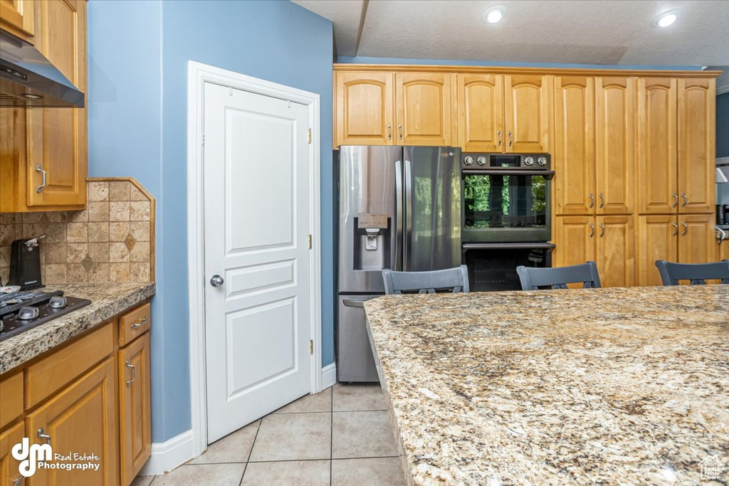 Kitchen featuring light stone counters, light tile patterned floors, a textured ceiling, backsplash, and black appliances